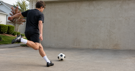 Un jeune joueur de football s'apprête à frapper un ballon contre un mur dans une allée.